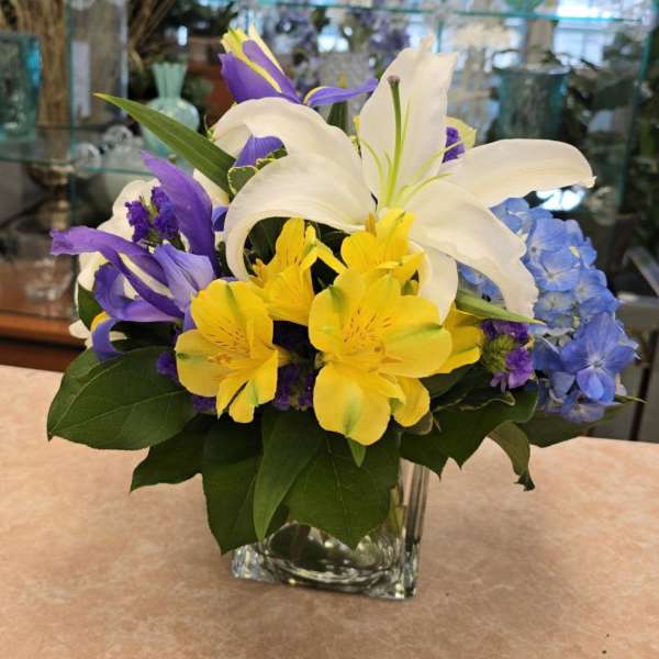 Mixed bouquet of white lilies, yellow alstroemeria, and purple iris in a glass vase
