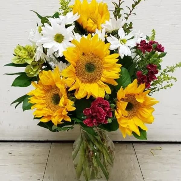 Bouquet of sunflowers, white daisies, and red flowers in a glass vase