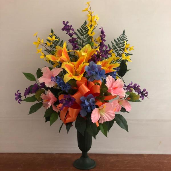 Tall silk arrangement of yellow lilies, pink and purple blooms, and blue flowers in a dark green pedestal vase