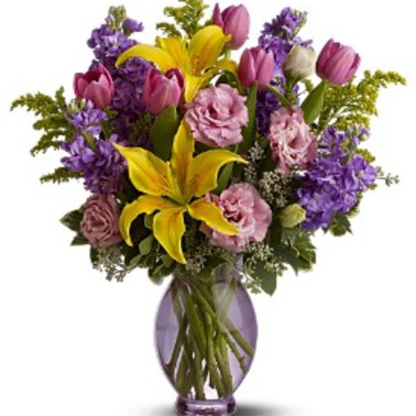 Bouquet of yellow lilies, pink tulips, and purple flowers in a glass vase