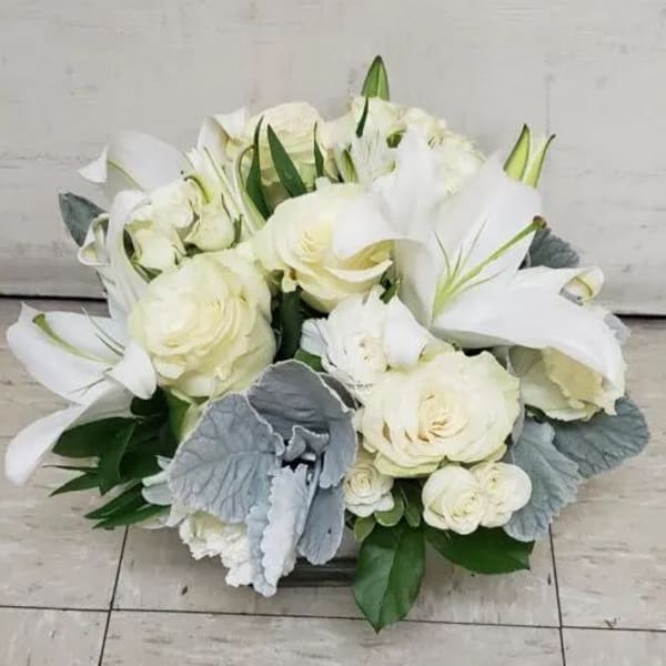 White roses and lilies arranged in a low bouquet with silver foliage