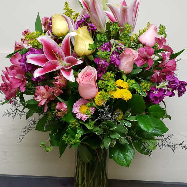 Mixed bouquet of pink lilies, roses, and yellow blooms in a glass vase