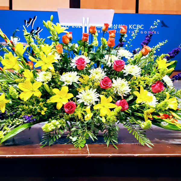 Large altar-style arrangement with yellow lilies, pink roses, and white mums on a stage
