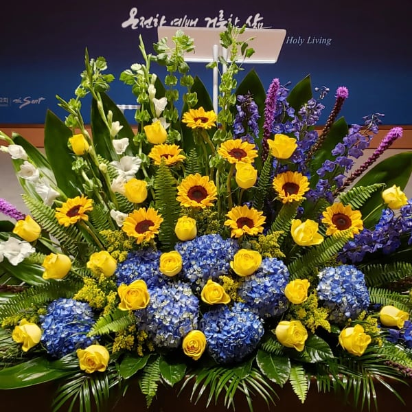 Large altar arrangement of yellow roses, sunflowers, blue hydrangeas, and tall purple accents