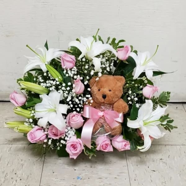 Low pink rose and white lily arrangement with a teddy bear and pink ribbon in the center
