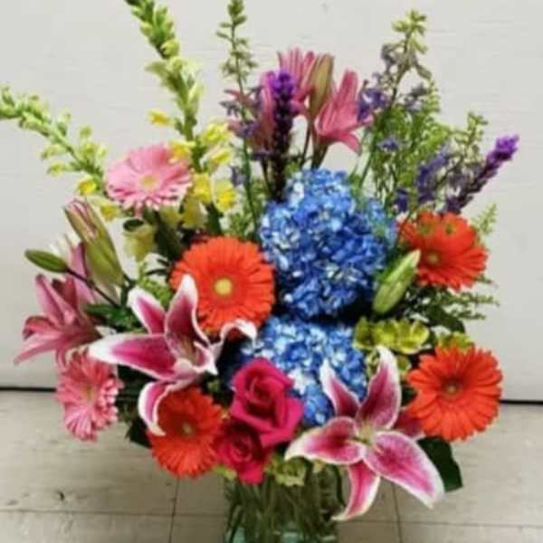 Colorful mixed bouquet in a glass vase with lilies, gerberas, roses, and hydrangeas