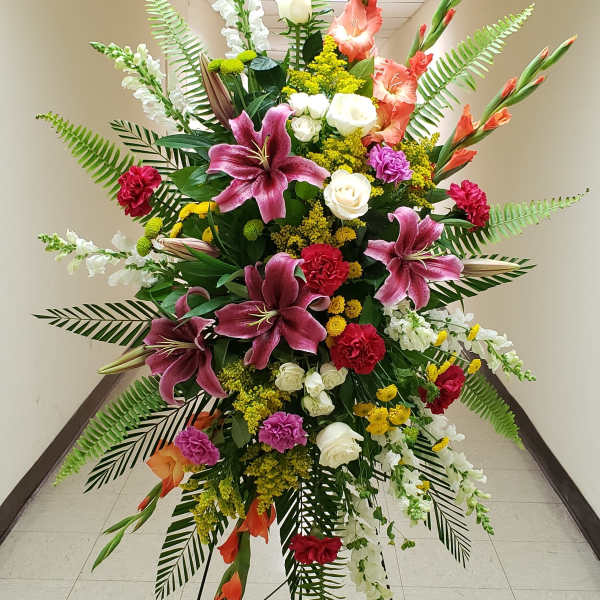 Tall standing spray of pink lilies, red carnations, white roses and mixed flowers on a metal easel