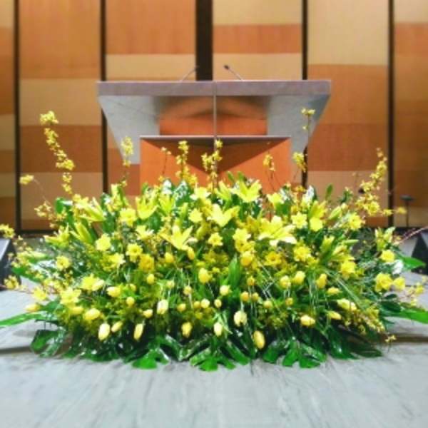 Large low arrangement of yellow lilies and tulips displayed on a stage in front of a podium