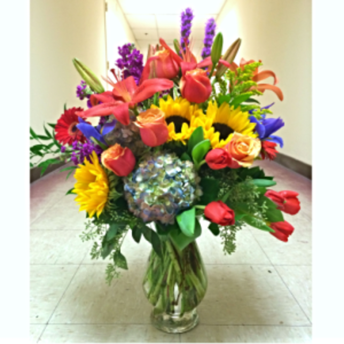 Colorful mixed bouquet in a clear glass vase with sunflowers and roses