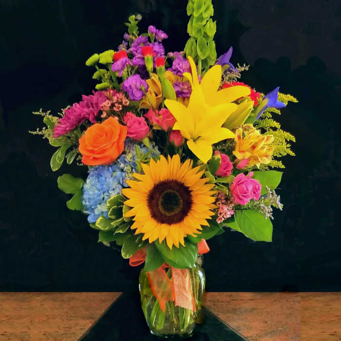 Colorful mixed bouquet with sunflower, lilies, roses, and hydrangea in a glass vase