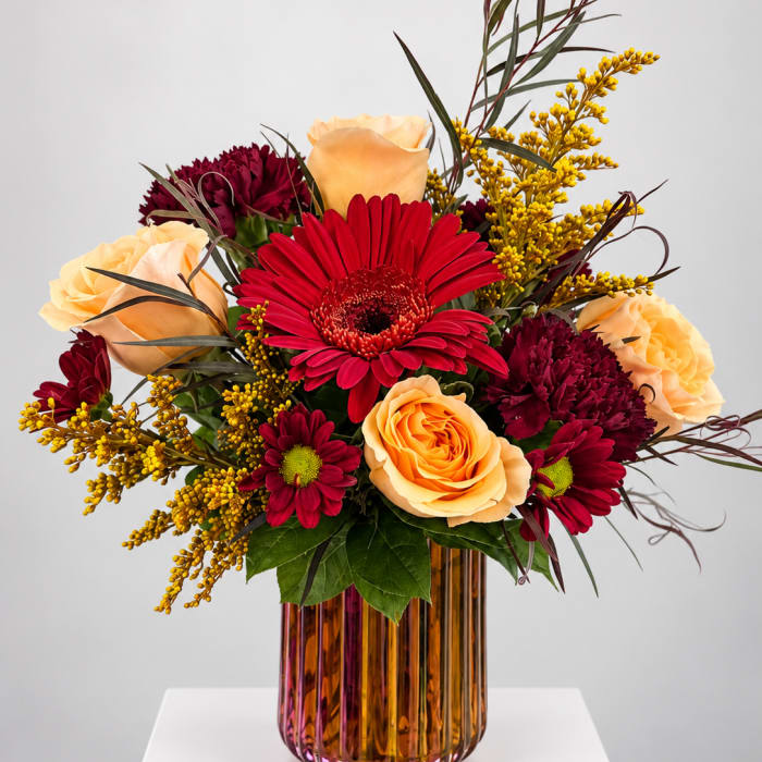 Mixed bouquet of red and peach flowers in an amber glass vase