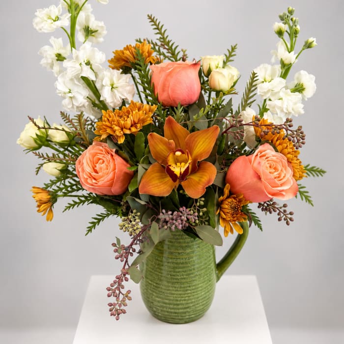 Peach roses and orange blooms in a green ceramic pitcher