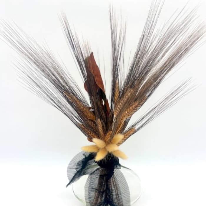 Decorative arrangement of dried grasses and feathers in a clear glass vase
