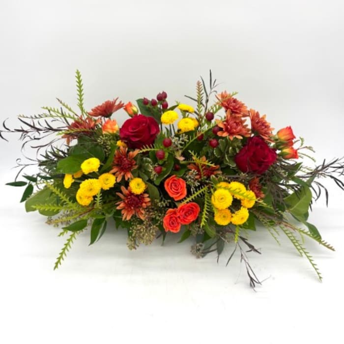 Low floral arrangement with red roses, orange blooms, and yellow pompons
