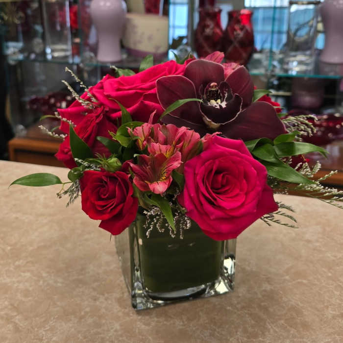 Pink and red roses with a dark orchid in a square glass vase