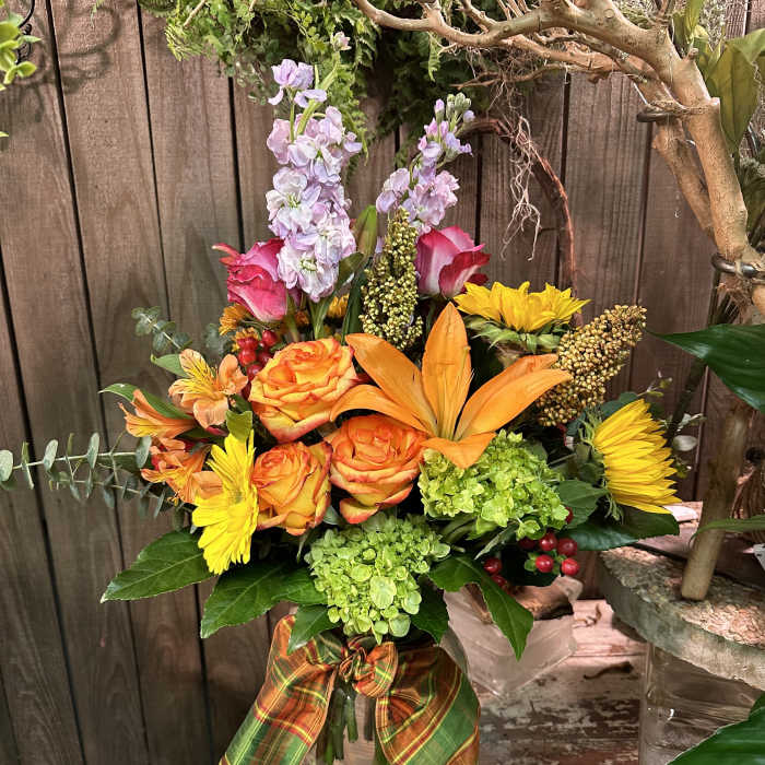 Mixed bouquet in a glass vase with orange roses, yellow daisies, and lavender spikes
