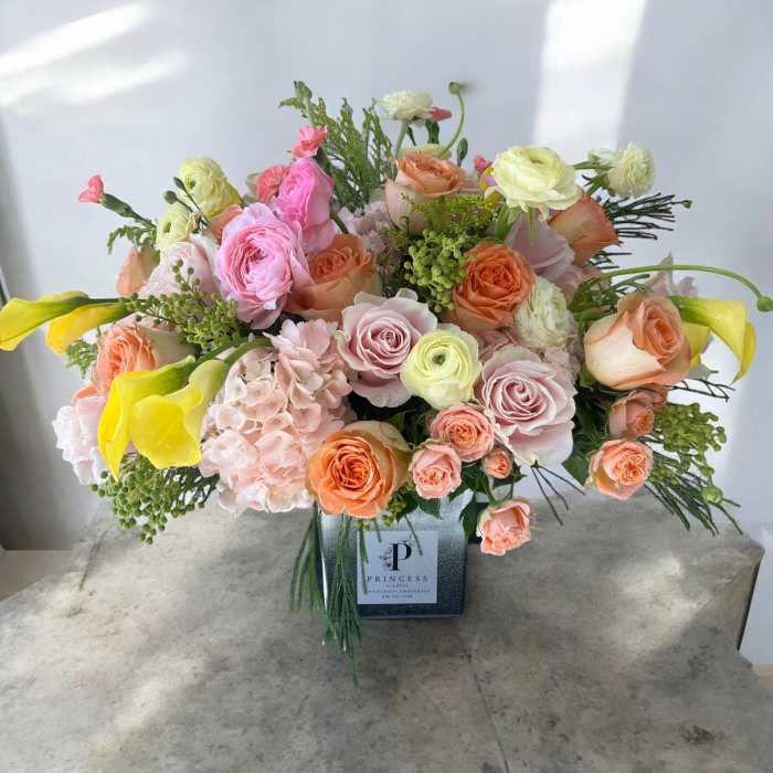 Mixed bouquet of pink, peach, and yellow flowers in a square vase