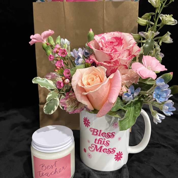Pink and peach flower arrangement in a mug with a candle beside it