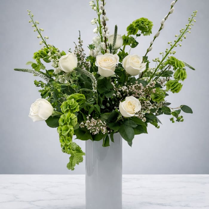 White roses and green blooms arranged in a tall glass vase