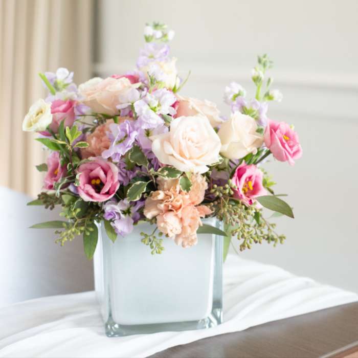 Low pastel arrangement of roses and lisianthus in a frosted glass cube vase on a draped table