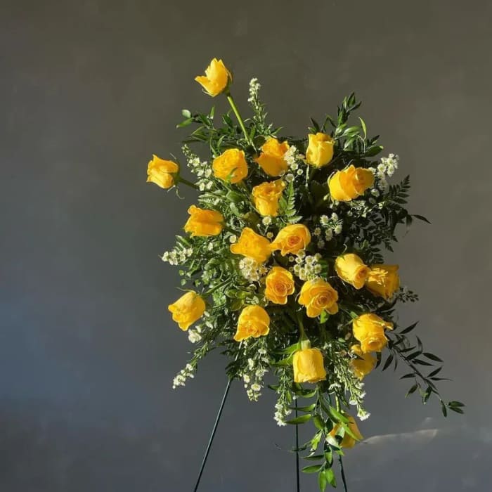 Yellow rose standing spray with white filler flowers on a black easel