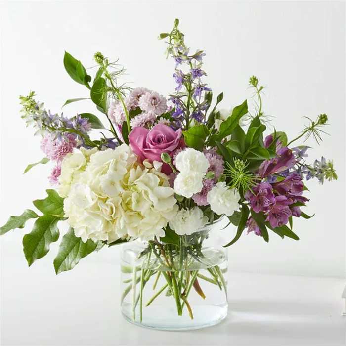 Mixed white and purple flower arrangement in a clear glass vase.