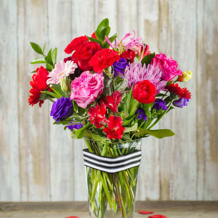 Mixed bouquet of red, pink, purple, and white flowers in a clear vase