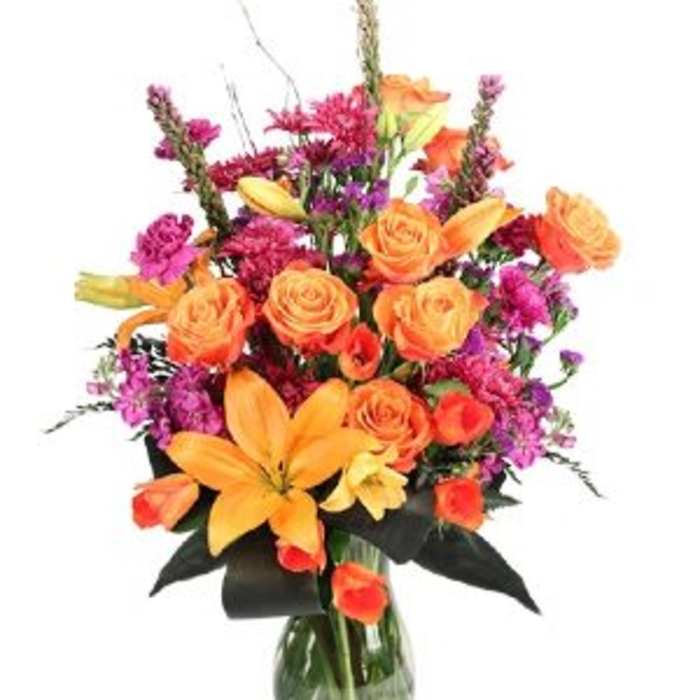 Orange roses and lilies in a glass vase with purple accents