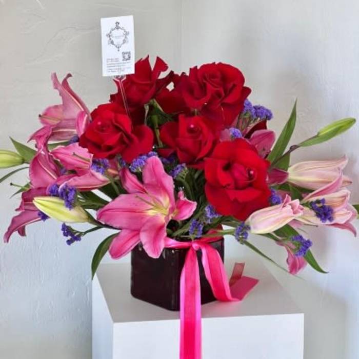 Red roses and pink lilies in a dark vase with a pink ribbon