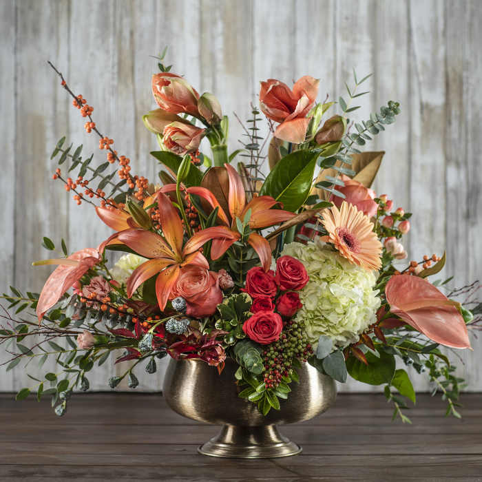 Coral lilies and red roses in a gold pedestal vase