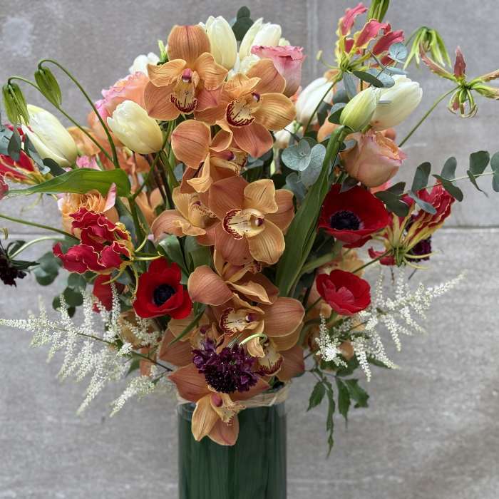 Mixed bouquet with orange orchids, red anemones, and pale tulips in a green vase