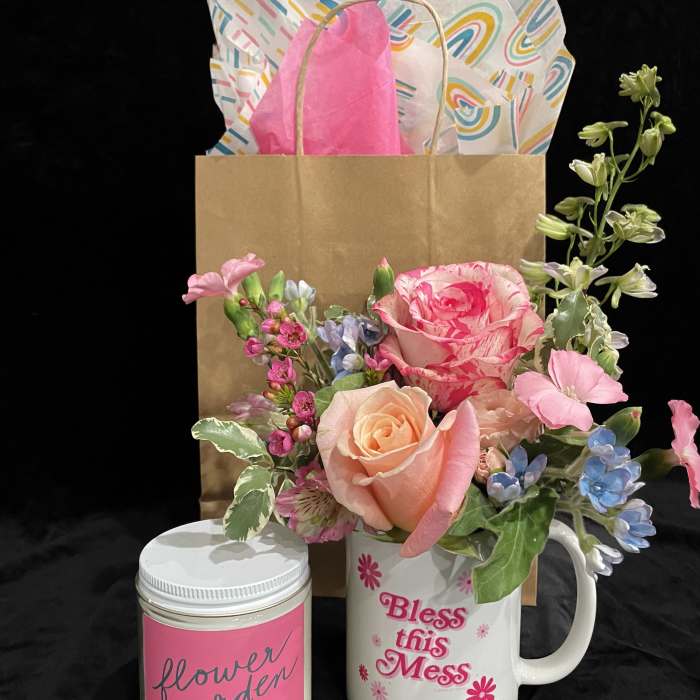 Pink and peach flower arrangement in a white mug with a candle and gift bag