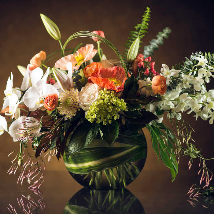 Mixed floral arrangement in a round glass vase with white orchids and orange poppies