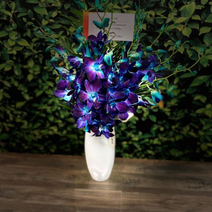 Purple and blue orchid arrangement in a white vase