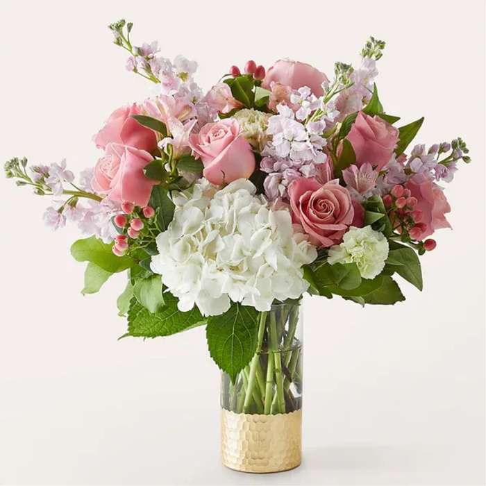 Pink and white mixed flower arrangement in a clear vase with a gold base