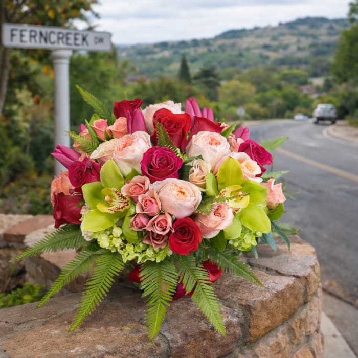 Bouquet of pink, red, and peach roses with green orchids