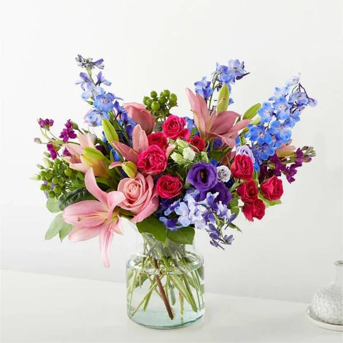 Mixed bouquet of pink lilies, roses, and blue delphinium in a clear glass vase