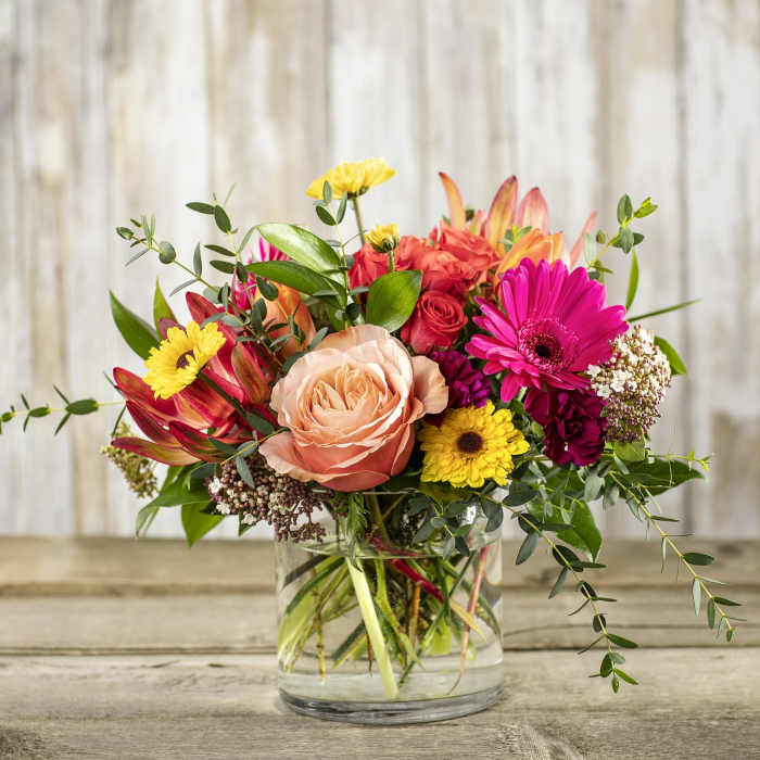 Mixed bouquet of roses, gerbera daisies, and other flowers in a glass vase