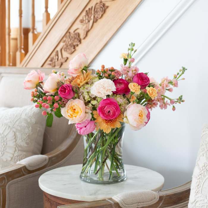 Mixed bouquet of pink, peach, and yellow flowers in a clear vase on a small table between chairs