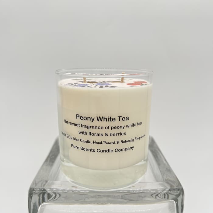 White scented candle labeled Peony White Tea in a clear glass jar on a glass stand