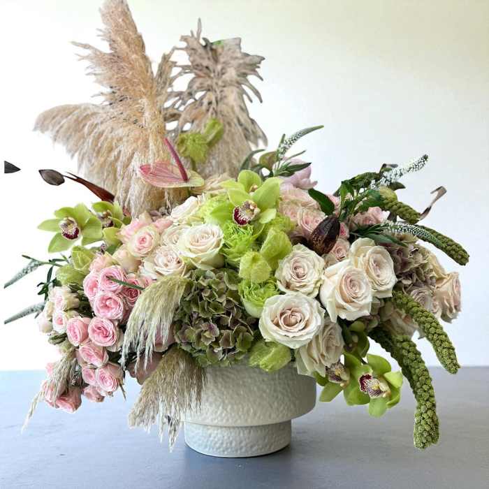 Low floral arrangement of roses, orchids, and green blooms in a white vase