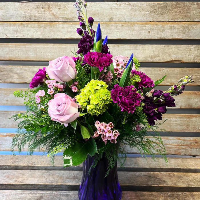 Mixed bouquet of pink roses, purple blooms, and green hydrangea in a purple vase