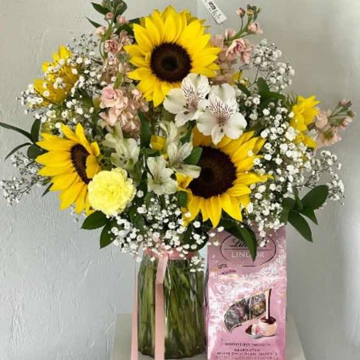 Bouquet of sunflowers and white flowers in a glass vase with a pink gift box