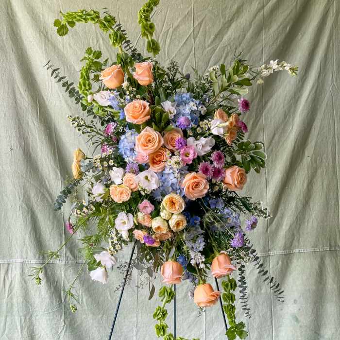 Tall floral spray with peach roses, blue hydrangea, and purple accents on a stand
