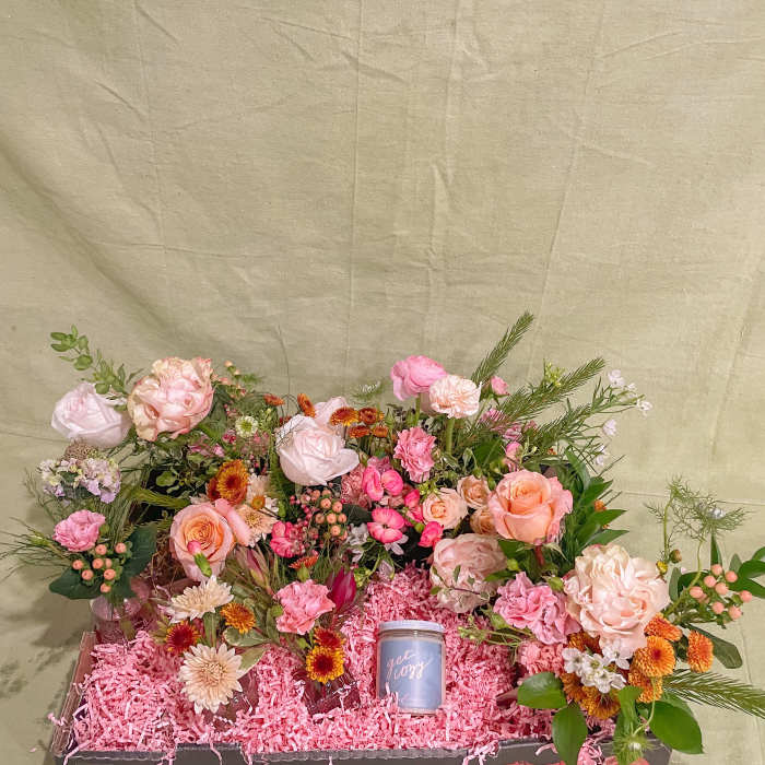 Mixed pink and peach flower arrangement in a gift box with a small candle