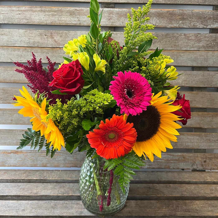 Mixed bouquet of sunflowers, gerbera daisies, and roses in a glass vase
