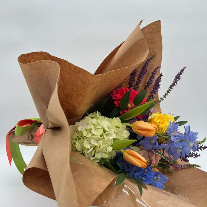 Wrapped bouquet of mixed hydrangea, tulips, roses, and blue flowers in kraft paper