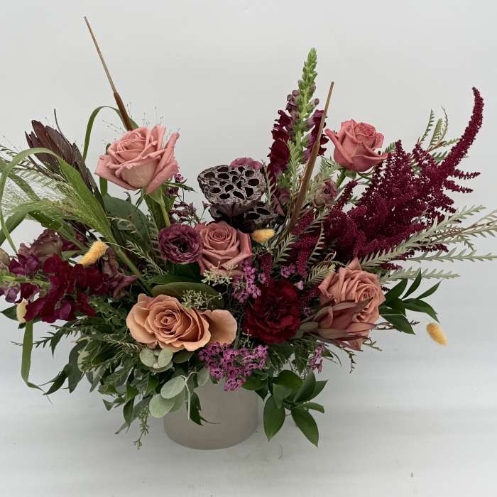 Mixed bouquet of pink roses and burgundy flowers in a white vase