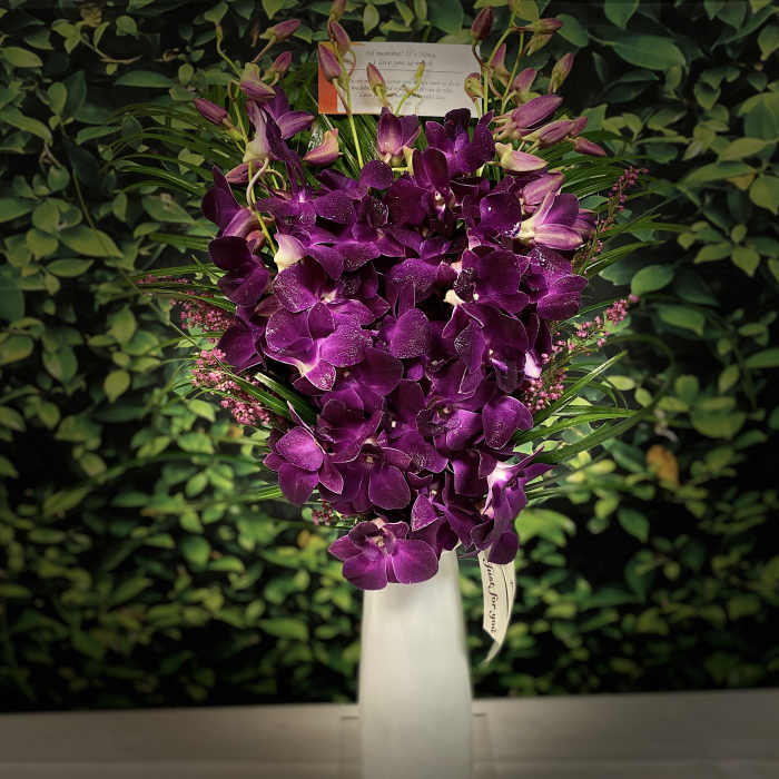 Purple orchid arrangement in a tall white vase