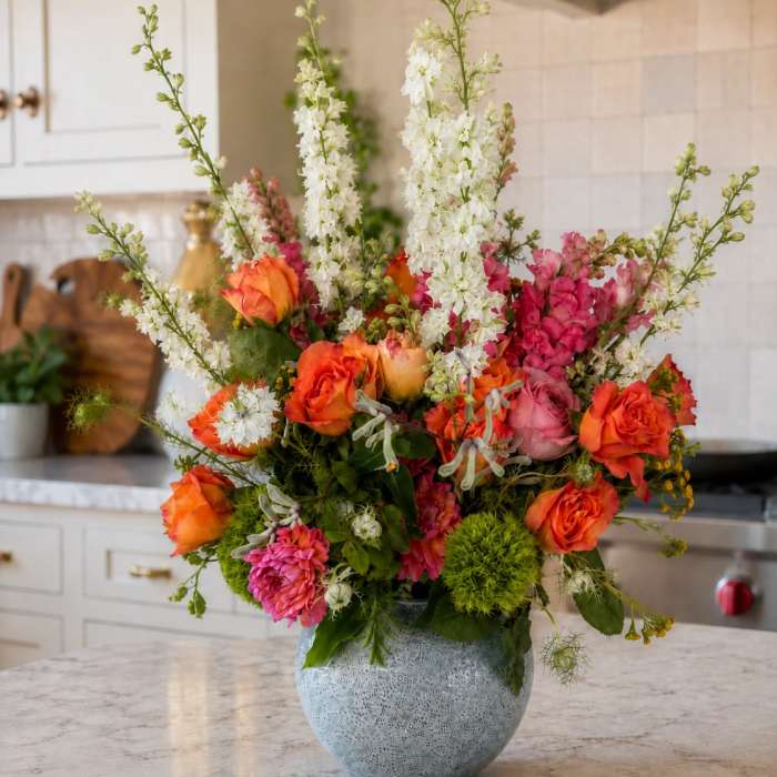 Colorful bouquet of orange roses, pink blooms, and white spikes in a blue vase